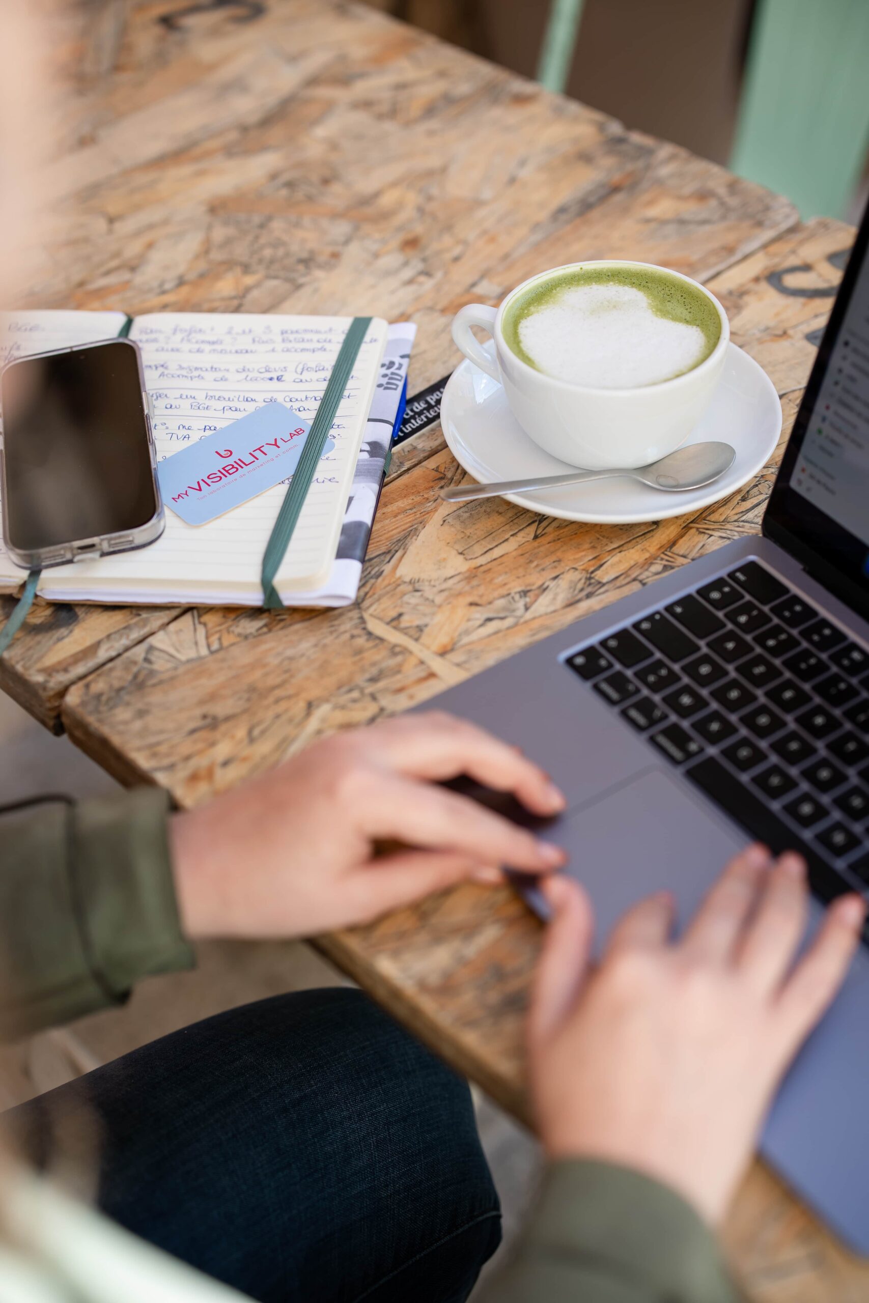Zoom sur les mains de Laura, créatrice de My Visibility Lab en train de travailler sur son ordinateur, à la terrasse d'un café.